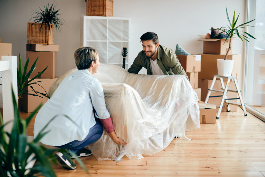 Two men are setting a couch in the middle of a room.